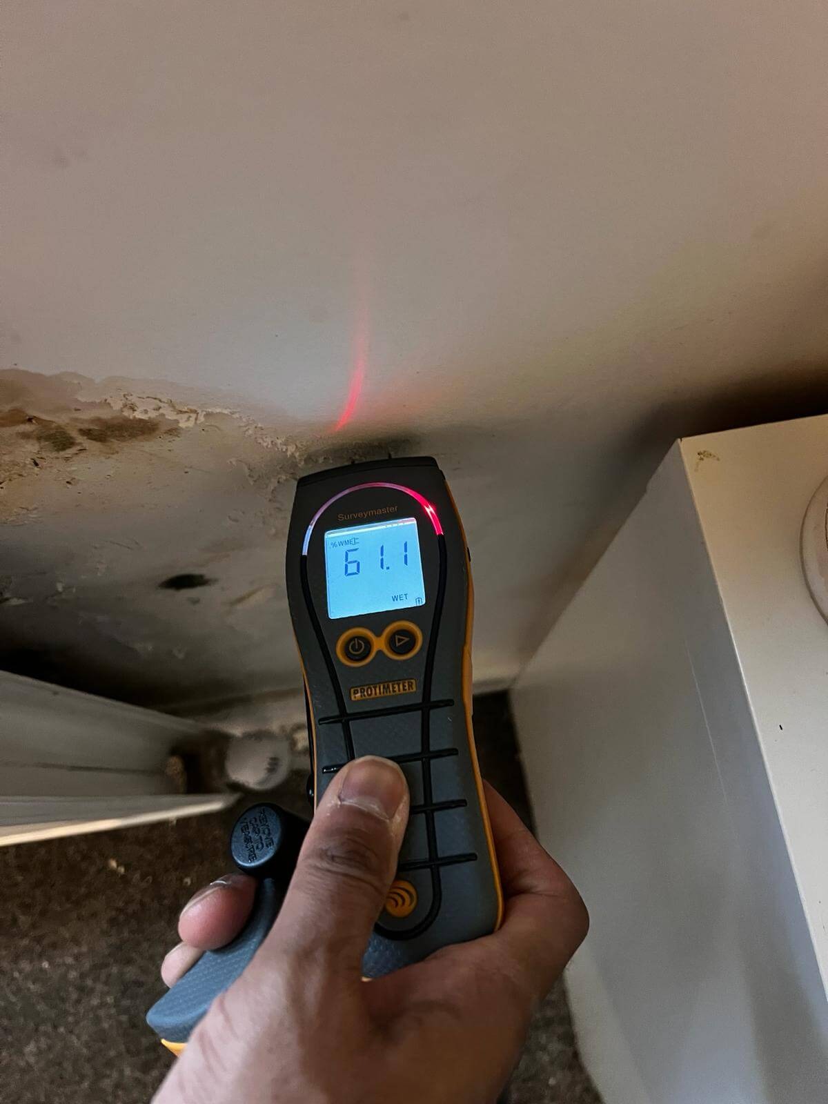 Handheld meter checking a marked ceiling beside cabinetry