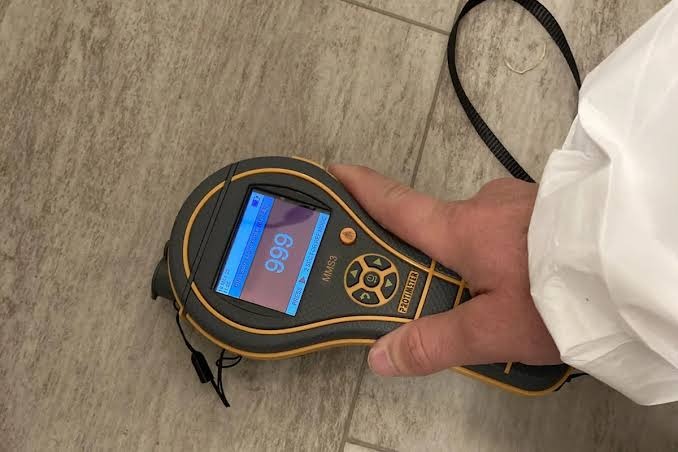 Handheld moisture meter being used to assess flooring